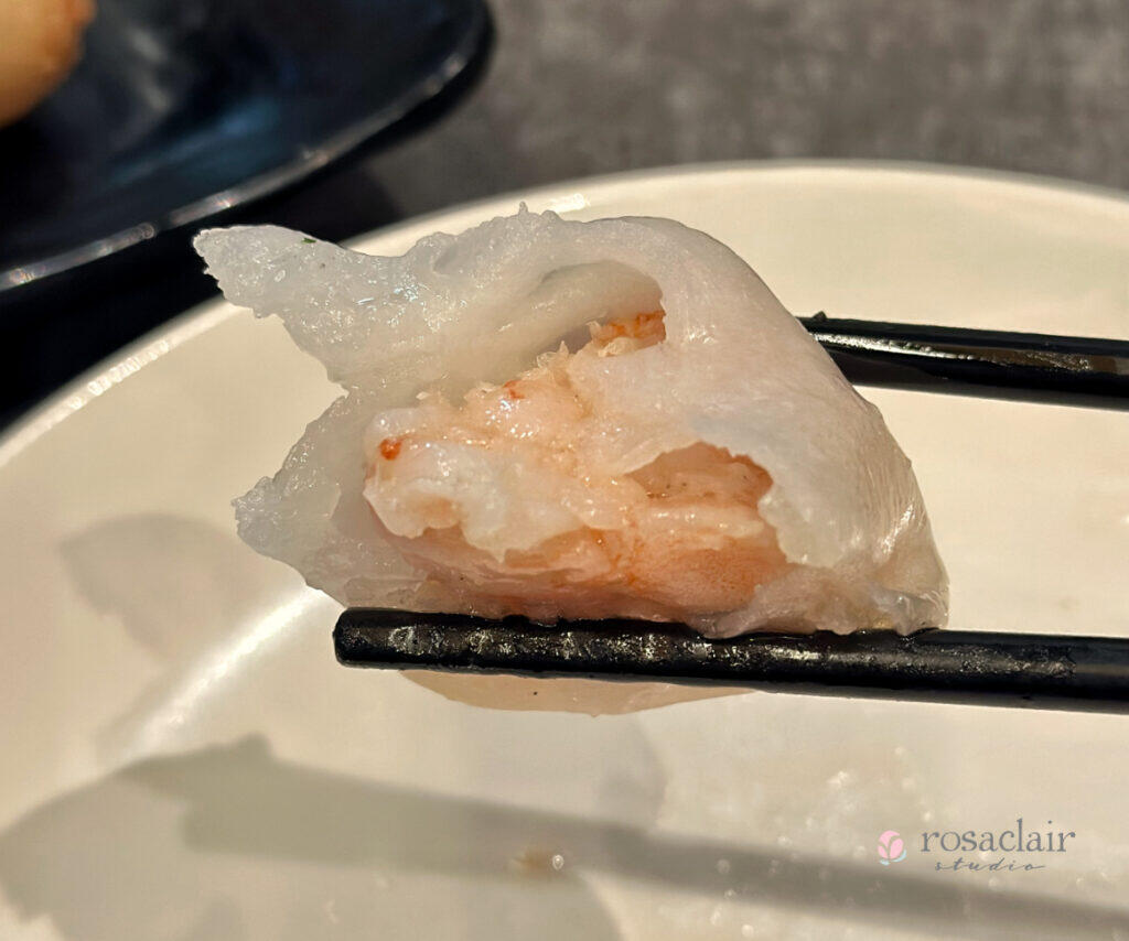 A pair of chopsticks holding a half-eaten Hargaw to show the shrimp filling